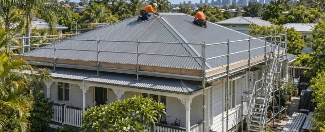 Illustration of two roofers installing a metal roof on a Queenslander home surrounded by scaffolding.